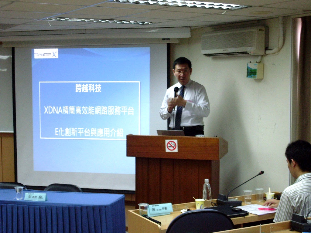 李奇申在產業電子化運籌管理學會演講，投影幕上顯示「跨越科技 XDNA 精簡高效能網路服務平台 E化創新平台與應用介紹」