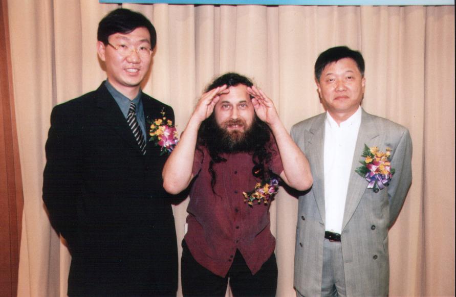 Richard Stallman 與李奇申、IBM 代表在活動現場合影，三人皆別胸花